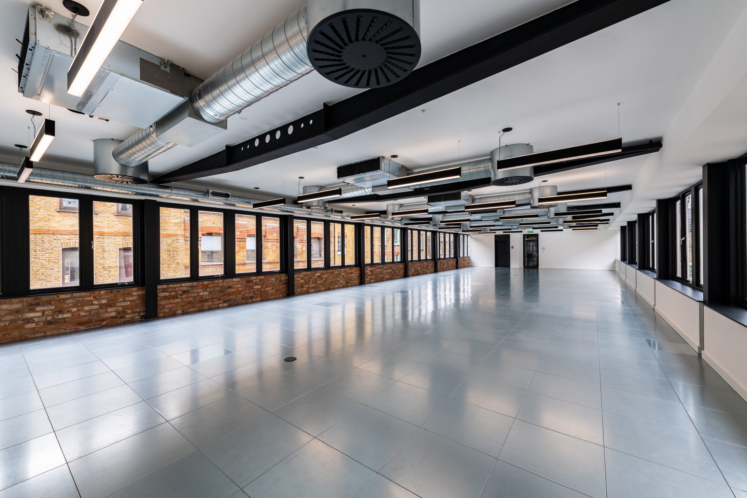 RFP_3425 grey tiled floor, low white ceilings, bright lighting ,industrial ducting, wall of windows with black frame and the lower quarter is a brick wall