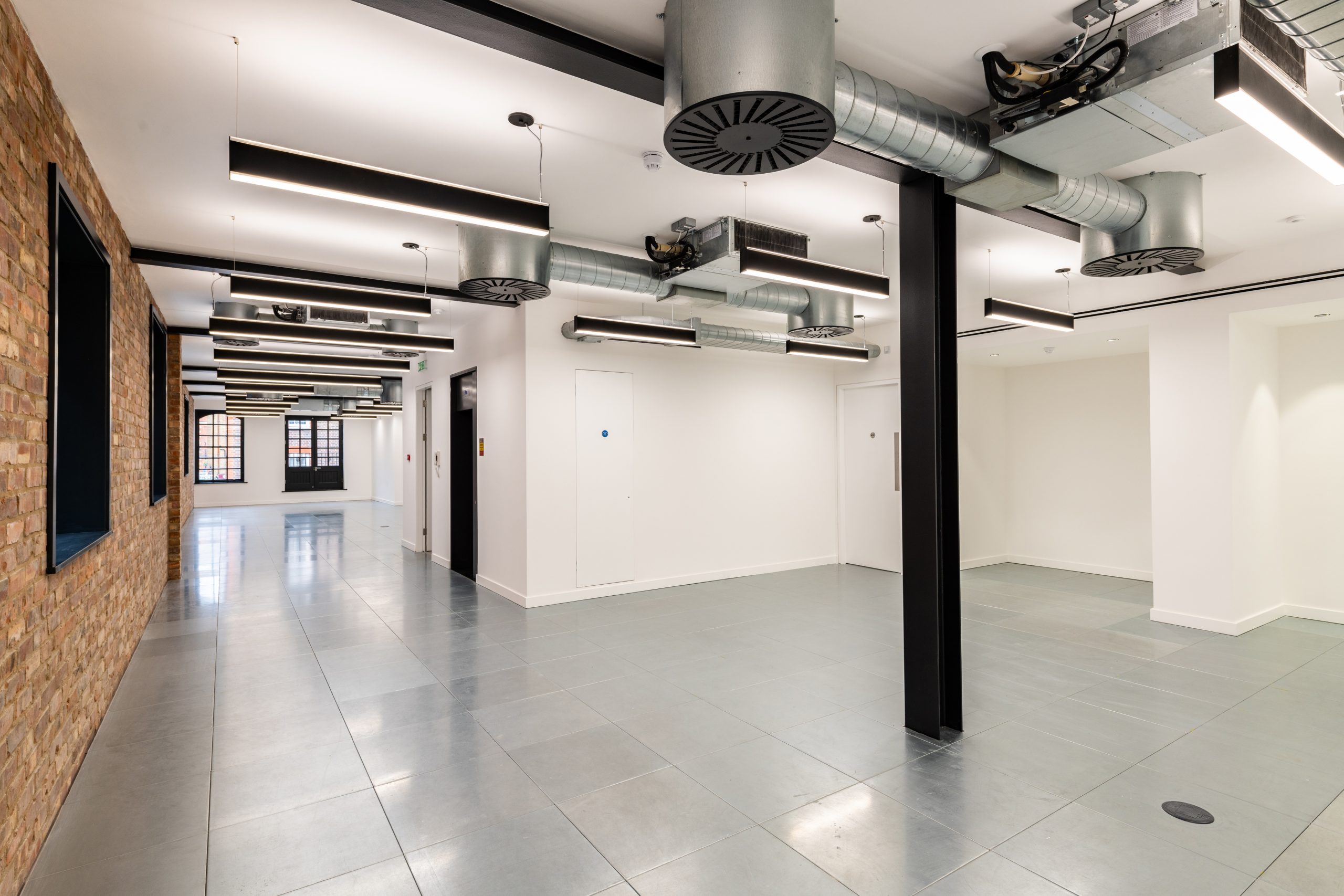 RFP_3491 office grey tiled floor internal brick wall black window frames low ceiling industerial ducting lots of bright lighting